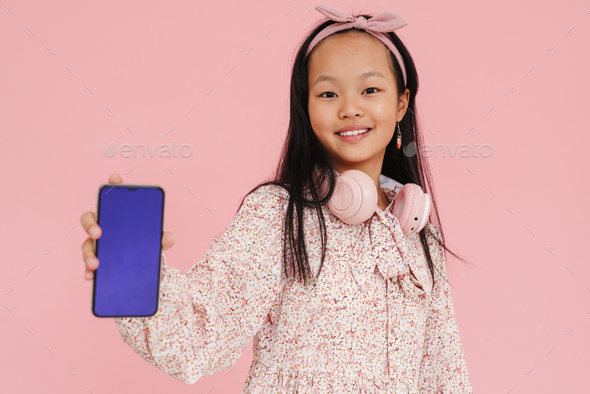 Asian girl wearing dress smiling while showing mobile phone - Stock Photo - Images