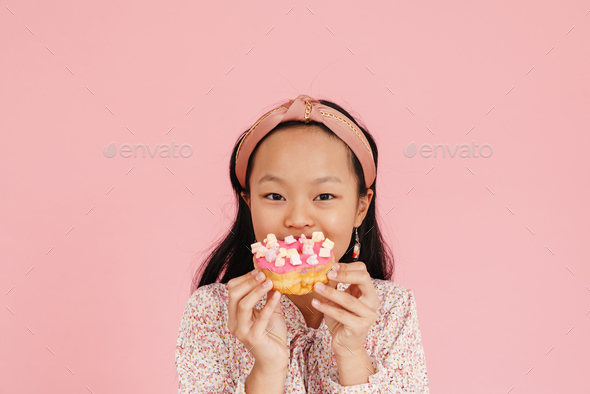 Asian girl wearing headband smiling while eating doughnut - Stock Photo - Images