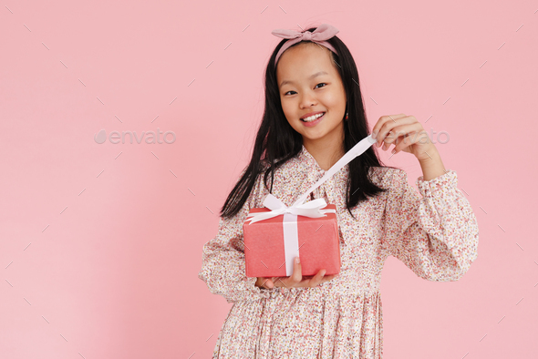 Asian girl wearing dress smiling while opening gift box - Stock Photo - Images
