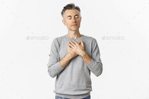 Image of handsome middle-aged male model with gray hair, holding hands on heart and thinking about