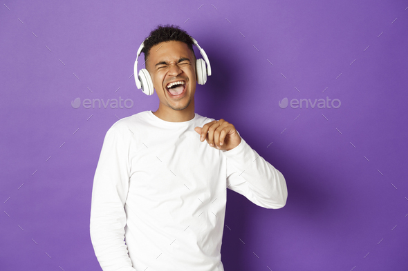 Image of carefree african-american guy dancing, listening music in wireless headphones and singing