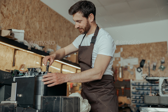 Handsome young man repairing coffee machine in a workshop