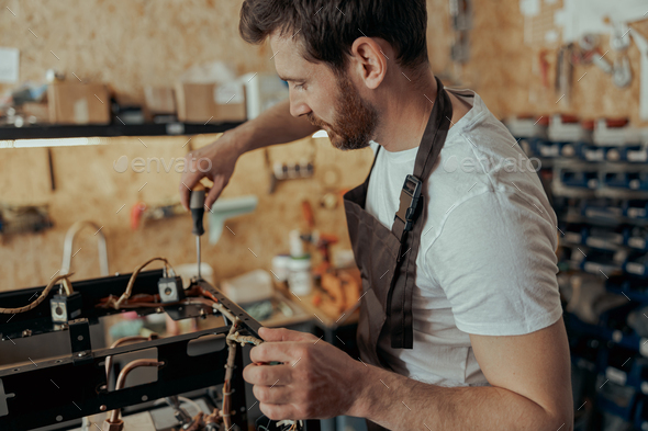 Smiling young man repairing coffee machine in a workshop