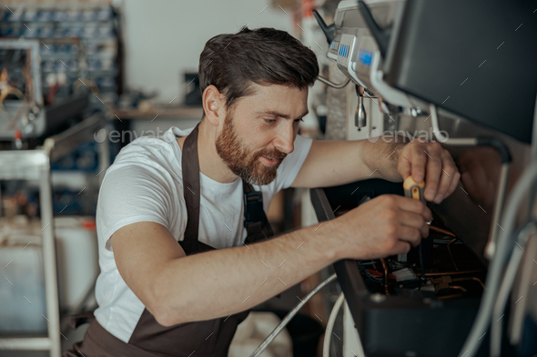 Smiling young worker repairing coffee machine in a workshop