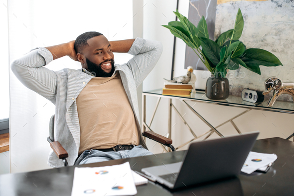 Happy calm african american man, freelancer, company employee, sits at the workplace in the office