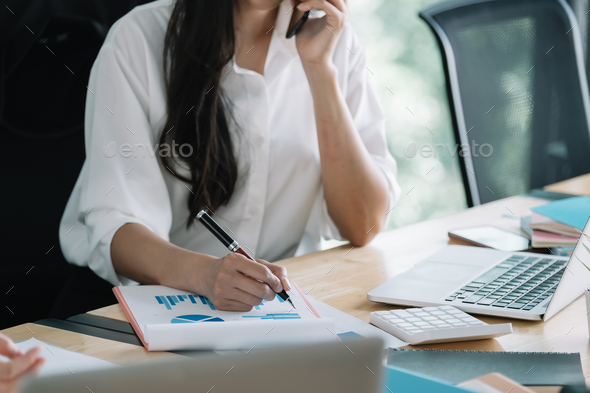 Young accountant hand holding smartphone to call marketing consultants and using laptop computer to