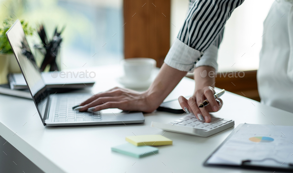 Close up Business woman using calculator and laptop for do math finance on wooden desk, tax