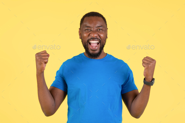 Joyful Black Guy Shaking Fists In Joy On Yellow Background