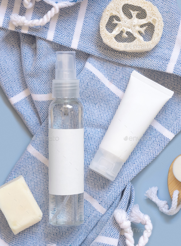 Cosmetic pump dispenser bottle and white cream tube on blue bath towel top view, mockup