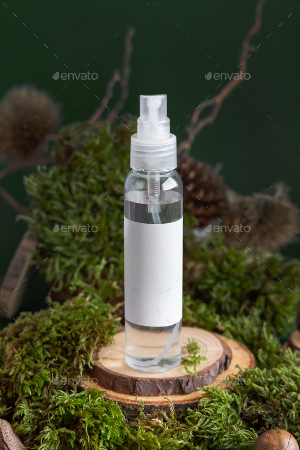 Refillable Cosmetic spray Dispenser on wooden piece near green moss, closeup. Label mockup