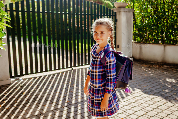 Girl with backpack ready to go to school and stands not far from home at first day after vacation