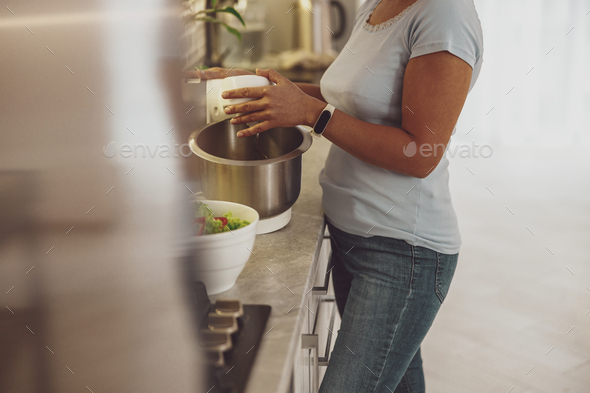 A housewife prepares dough with a dough mixer standing in the kitchen