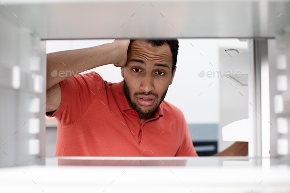 Starving hungry shocked disappointed young african american man checks empty fridge got stress in