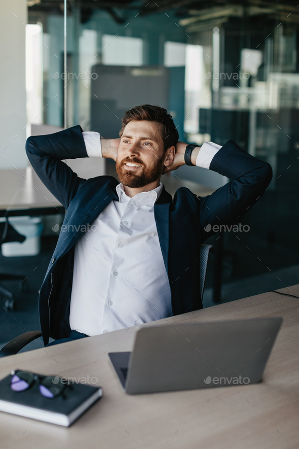 Taking break from work. Excited businessman relaxing on chair, leaning back at workplace and holding