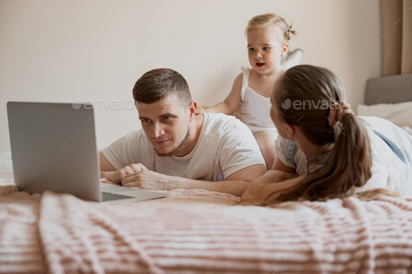 Cheerful family having fun together watching cartoons online on laptop lie on sofa at home