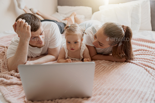 Happy family having fun together watching cartoons online on laptop lie on sofa at home