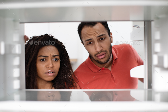 Hungry unhappy upset young african american woman and man check empty fridge in kitchen