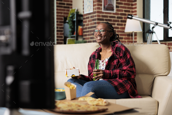 Smiling woman drinking bottle of beer and eating delivery meal