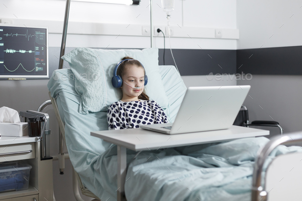 Ill little girl patient sitting in pediatric clinic bed while watching ...