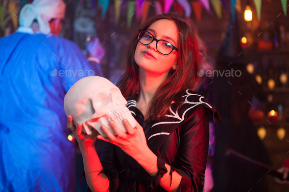 Pretty little girl dressed up like a witch holding a human skull at halloween party