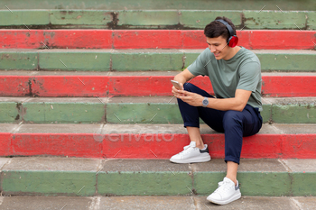 Latin man sitting on colorful stairs typical of Latin America, looking at his cell phone.