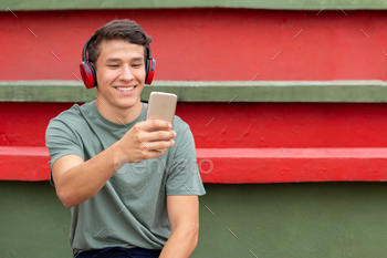 Young latin guy making a video call and wearing headphones with a big smile on his face.