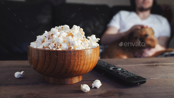 Wooden bowl with salted popcorn and TV remote on wooden table