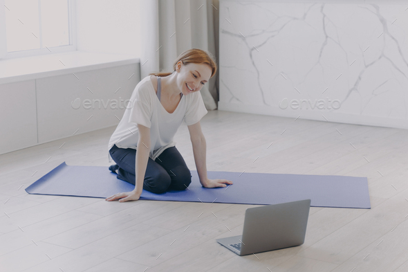 Happy caucasian woman has distance personal training in front of camera on yoga mat on floor.