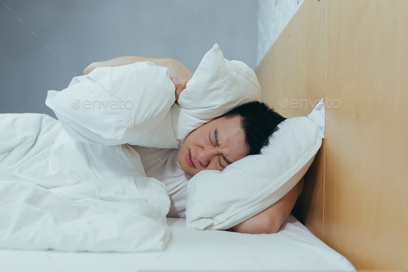 A man at home tries to fall asleep, noisy neighbors interfere with sleep