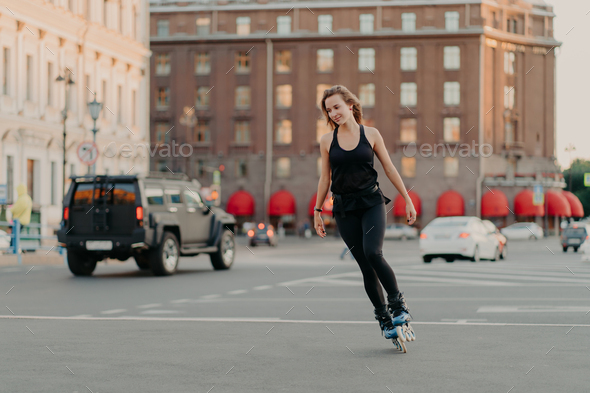 Active girl rollerblading on grey asphalt poses on rollers dressed in active wear