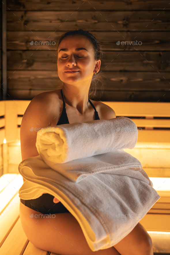 Young Woman in Towel Relaxing on Bench in Sauna Stock Photo