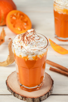 Spicy latte with pumpkin and whipped cream on wooden background