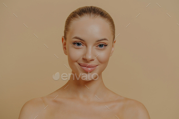 Beauty portrait of charming woman with healthy glowing skin posing seminude against beige wall
