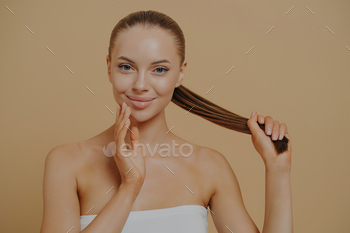 Beauty portrait of young naturally beautiful woman touching facial skin and holding hair in ponytail
