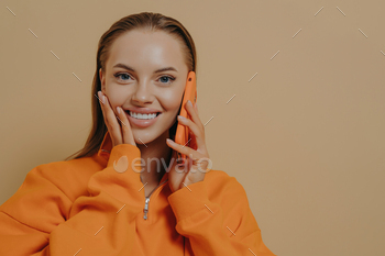 Happy excited woman talking on phone, hearing good news via mobile phone, isolated over beige wall