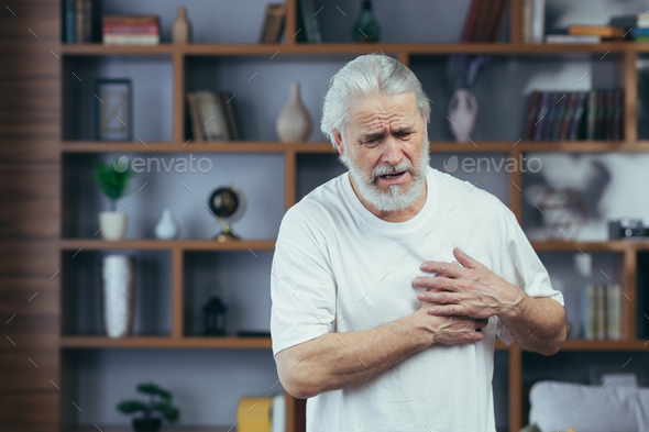 Gray-haired man has severe chest pain, grandfather\'s heart aches, holds hands on his chest, at home