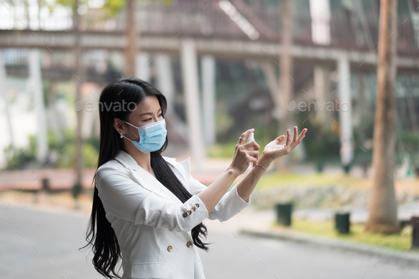 Portrait of businesswoman wearing mask sanitizing hands at post pandemic office, copy space.