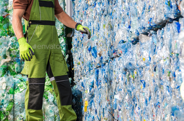 Waste Management Worker in Front of a Pile of Pressed Plastic PET Bottles