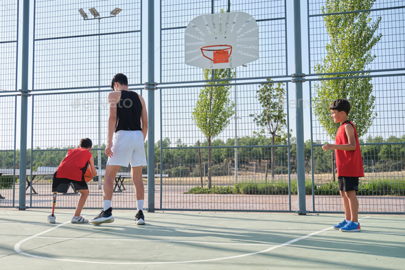 Basketball trainer playing basketball with two children, one of them has a leg prosthesis