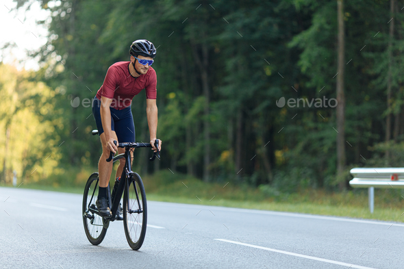 Happy cyclist in sport outfit riding bike among forest