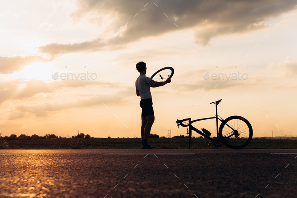 Muscular man in silhouette fixing wheel on bike