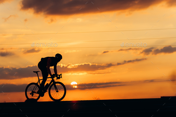 Muscular man biking on road during amazing sunset