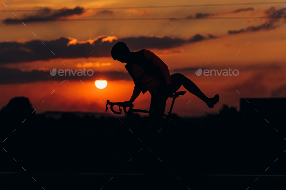 Muscular guy in silhouette having evening cycling on road