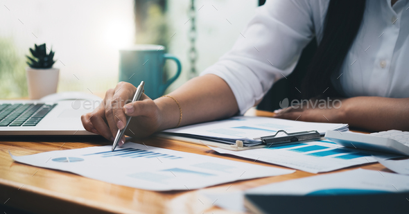 Business analyst working - hand with pen, calculator, coffee, magnifier, worksheet and graph