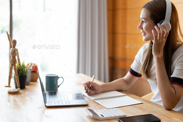 Young asian woman writing notes in notebook watching webinar video course, serious black male