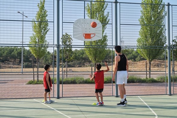 Basketball trainer showing how to shoot basketball to a two children.