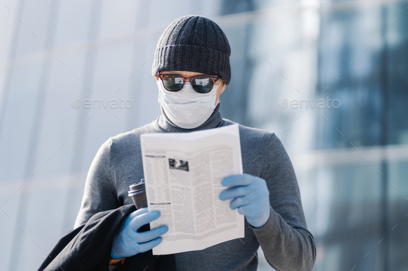 man reads article about coronavirus symptoms, wears protective medical mask and rubber gloves