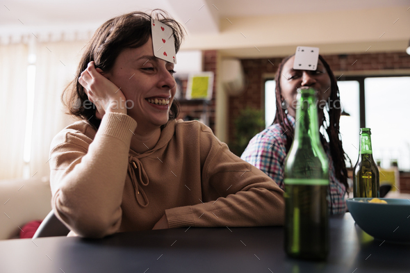 Smiling woman with card game on forehead enjoying society games with friends at home.