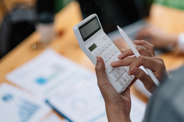 Woman entrepreneur using a calculator with a pen in her hand, calculating financial expense with - Stock Photo - Images