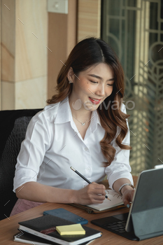 Portrait charming asian woman taking note on notepad while video conference via digital tablet